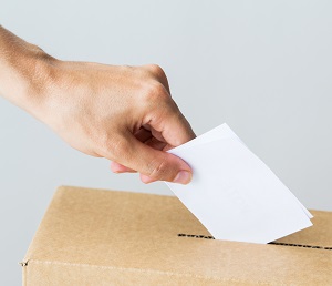A hand placing a voting slip into a box