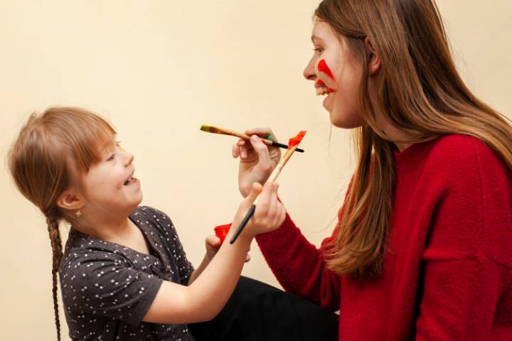 A girl and adult smiling, painting each others faces.