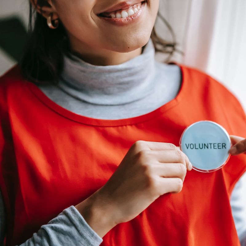 Woman smiling and showing off her volunteer badge pinned to her apron.