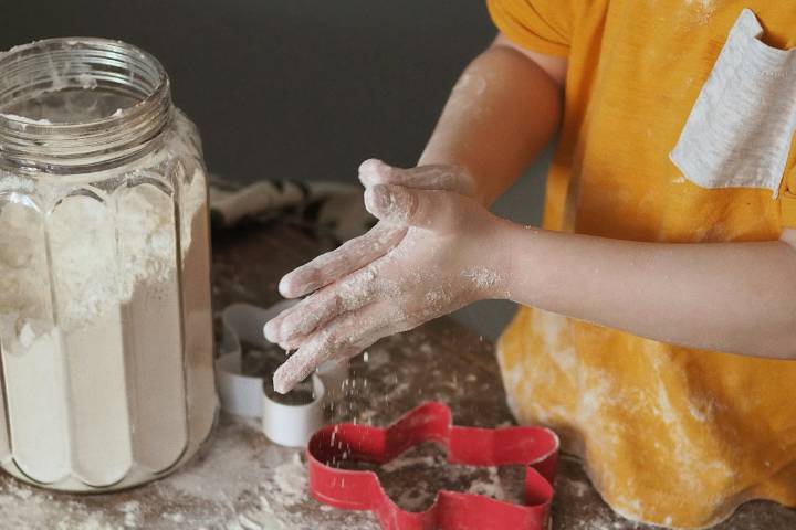 A child&#039;s hands covered in flour. They are rolling dough between their hands to make gingerbread.