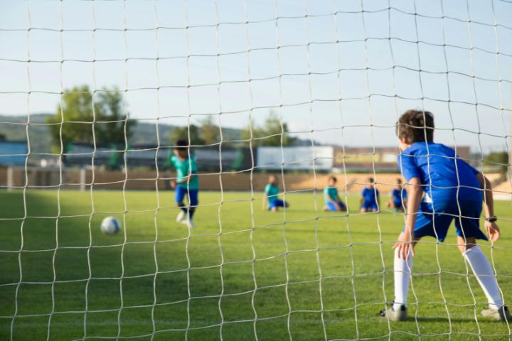 A child playing football as the goalie. He is guarding the net.