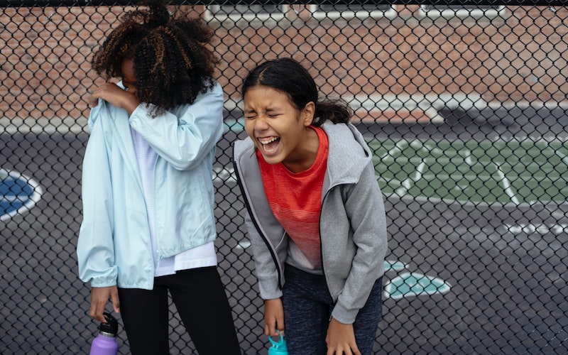 Two girls outdoors in sports clothing and laughing together.