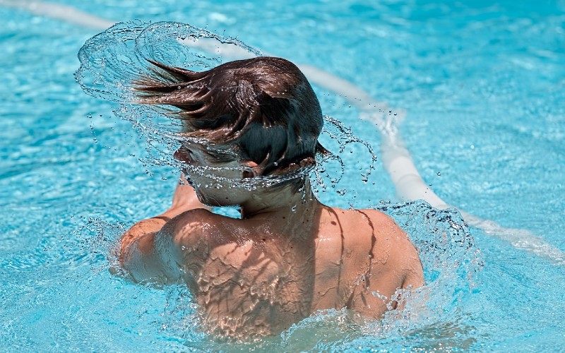 Boy splashing in swimming pool.