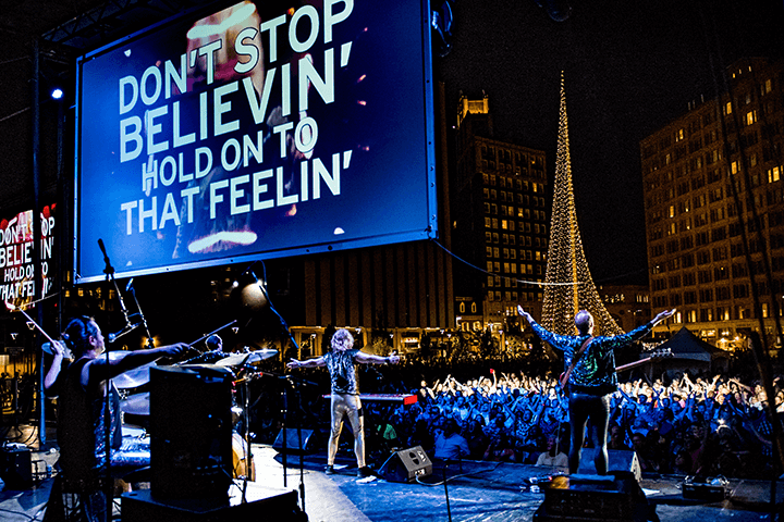 A live Massaoke performance with the words "Don't stop believin' hold on to that feelin" on a large digital screen.