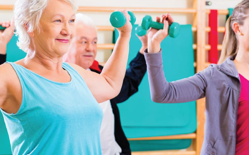 Exercise class sat on floor using dumbbells in their arms.