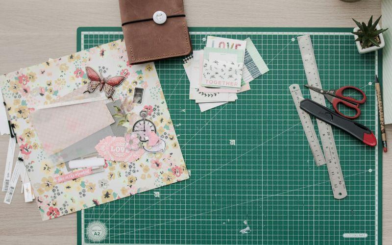 Card making equipment and floral card design on a green cutting mat.