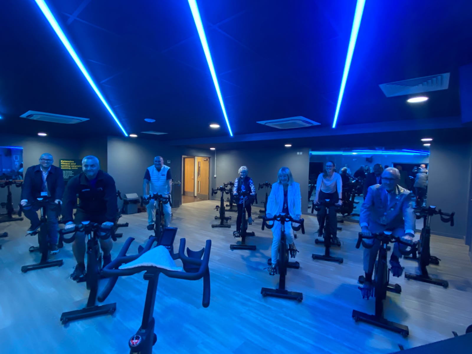 A group of people smiling and posing atop spinning bikes, in a new state of the art spinning studio