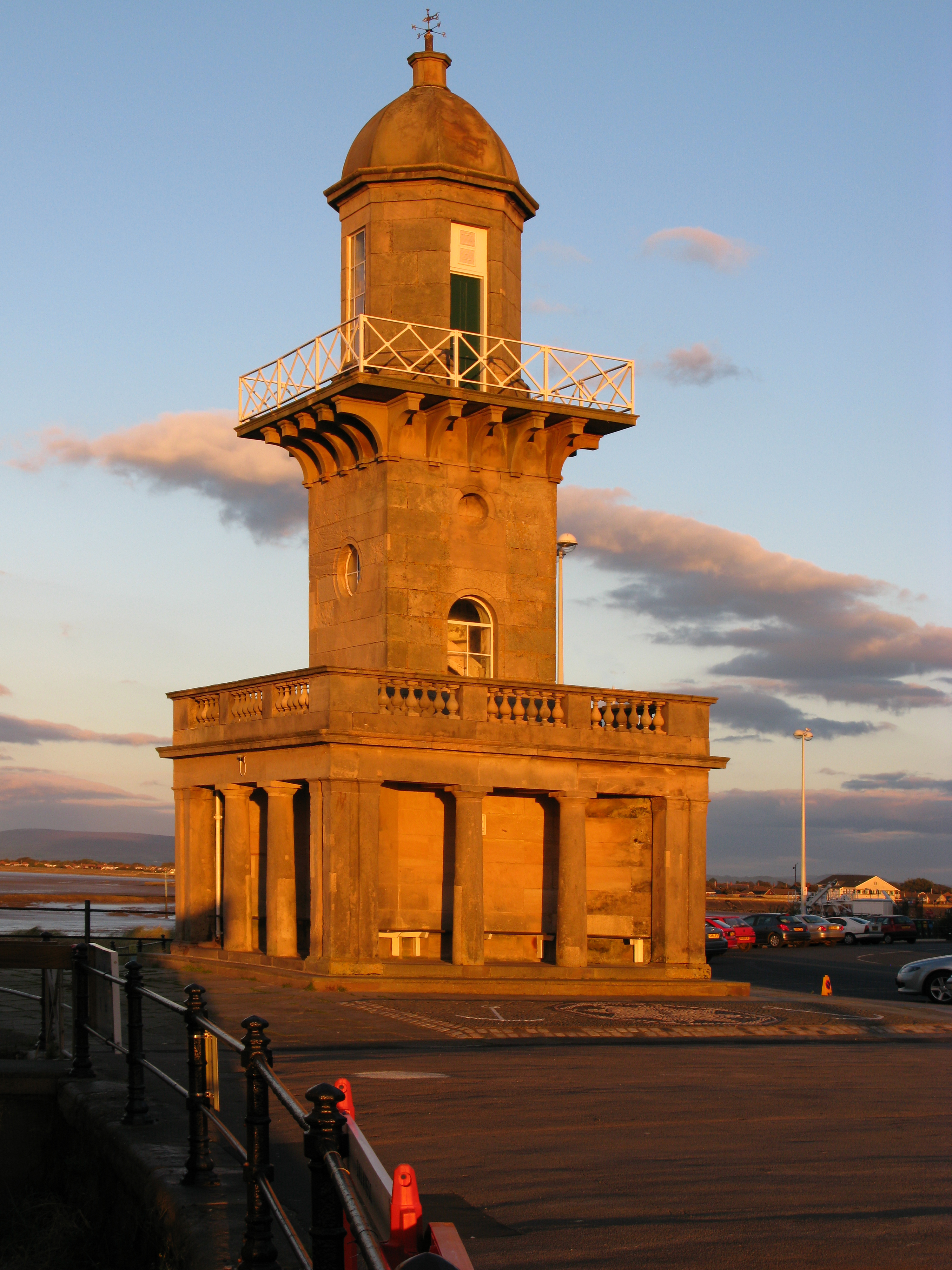 Lighthouse at sunset. A tall building with a domed room and pillars at the bottom.