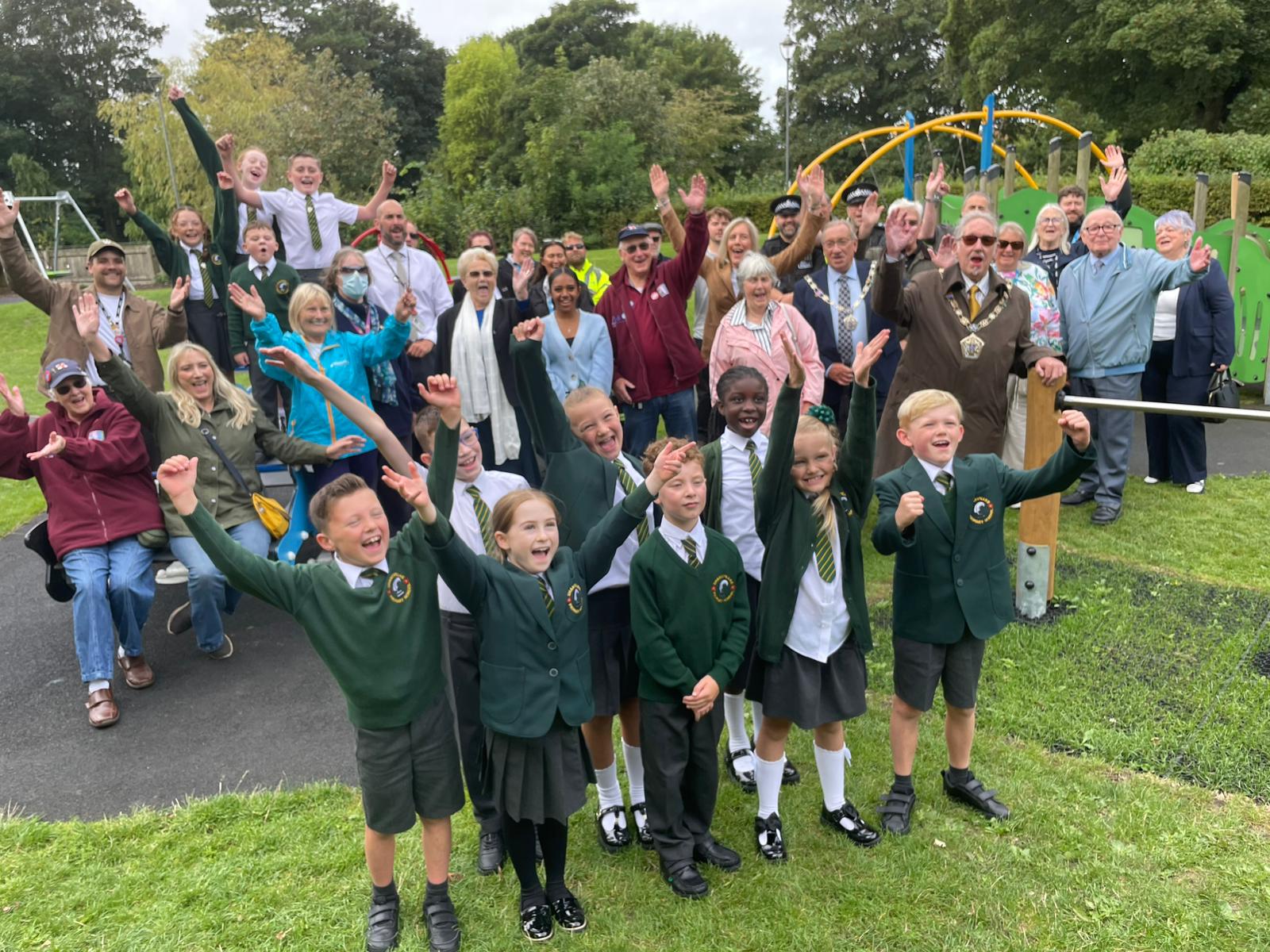 A group of children and adults celebrating the opening of new playground equipment.