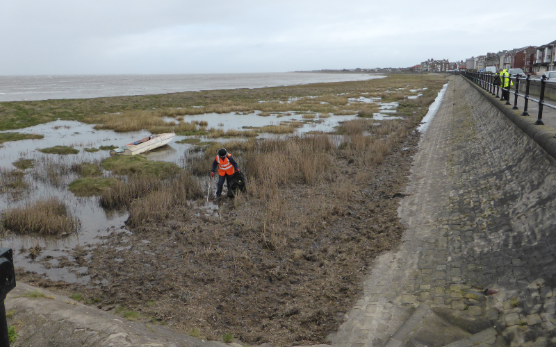 Man in orange vest cleaning Knott End beach.