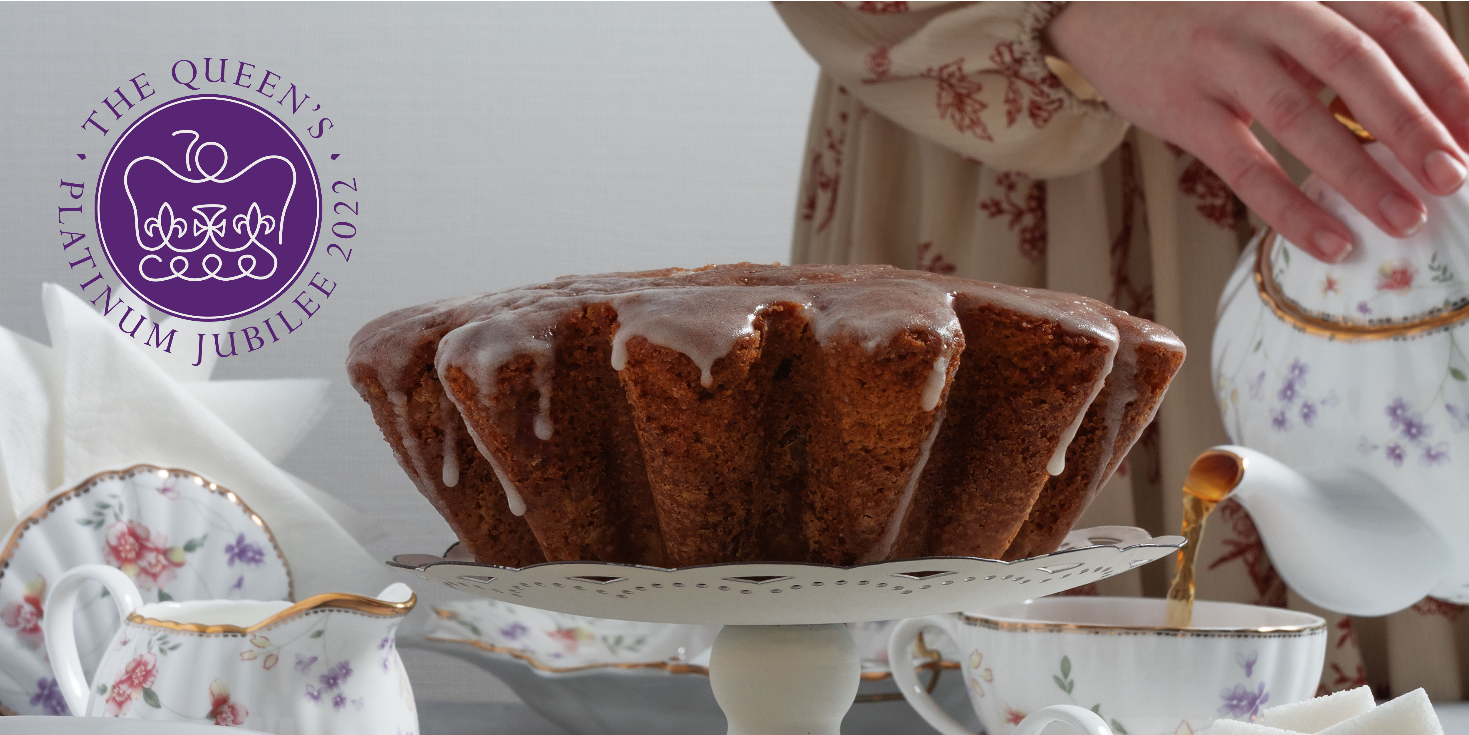 Image of a cake on a cake stand and a woman pouring a cup of tea from a teapot