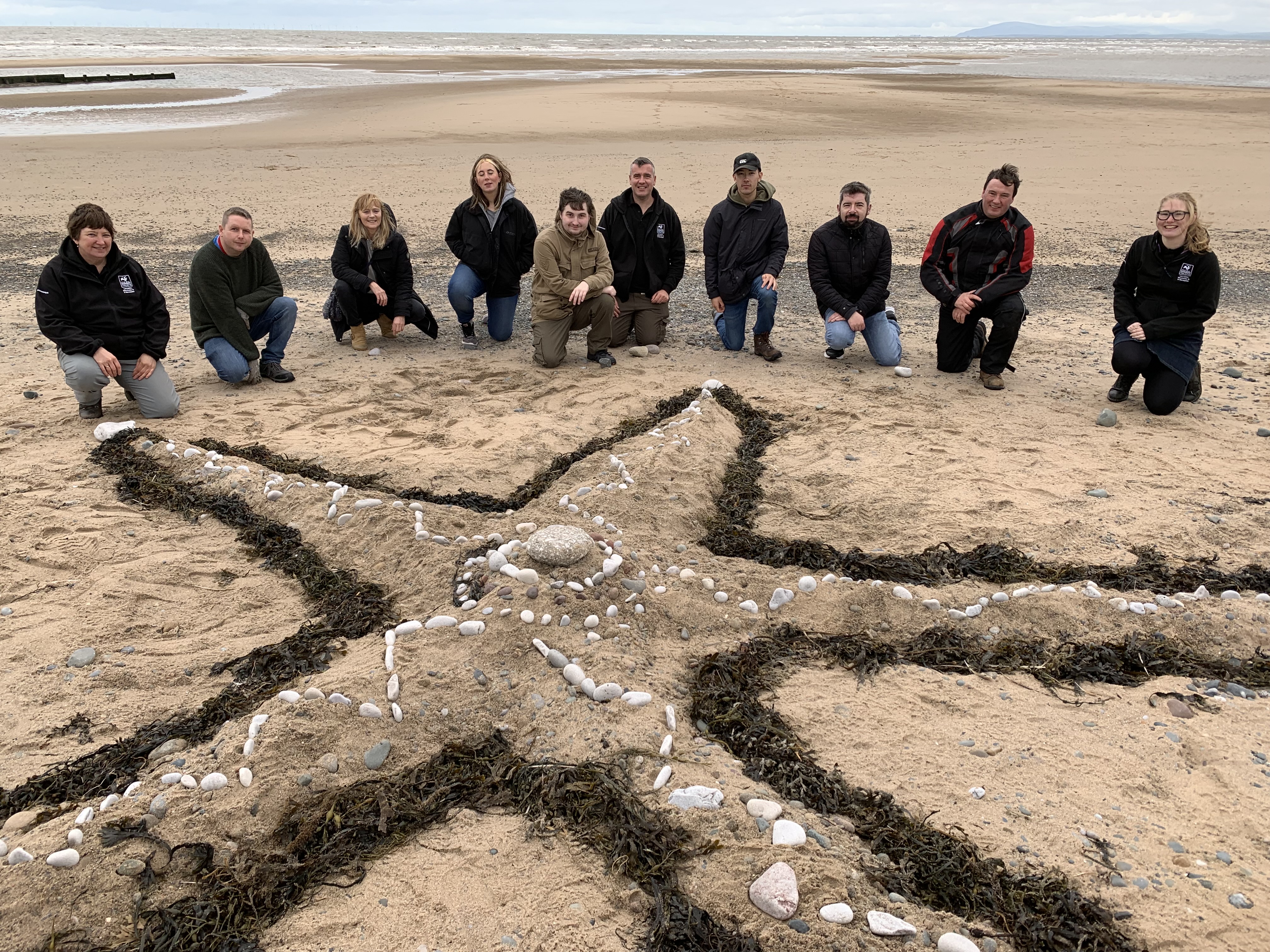 A group of people on a beach showing off a sand sculpture