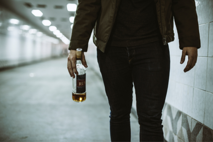Bottom half of man walking through tunnel carrying a bottle of rum