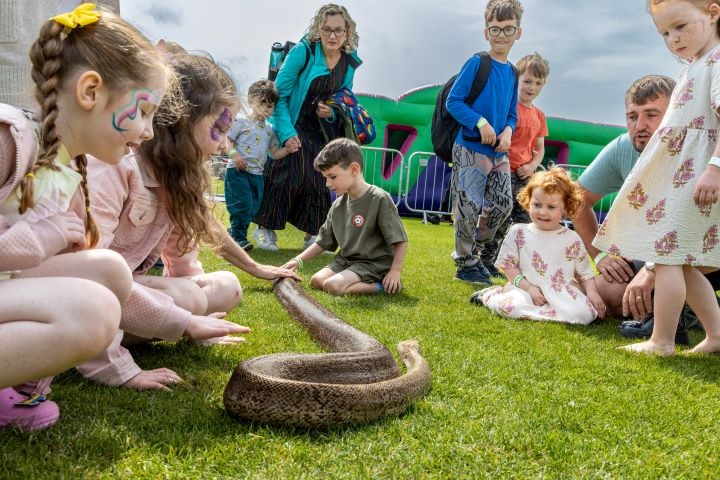 Children at Wanderland 2025 petting a giant anaconda snake.