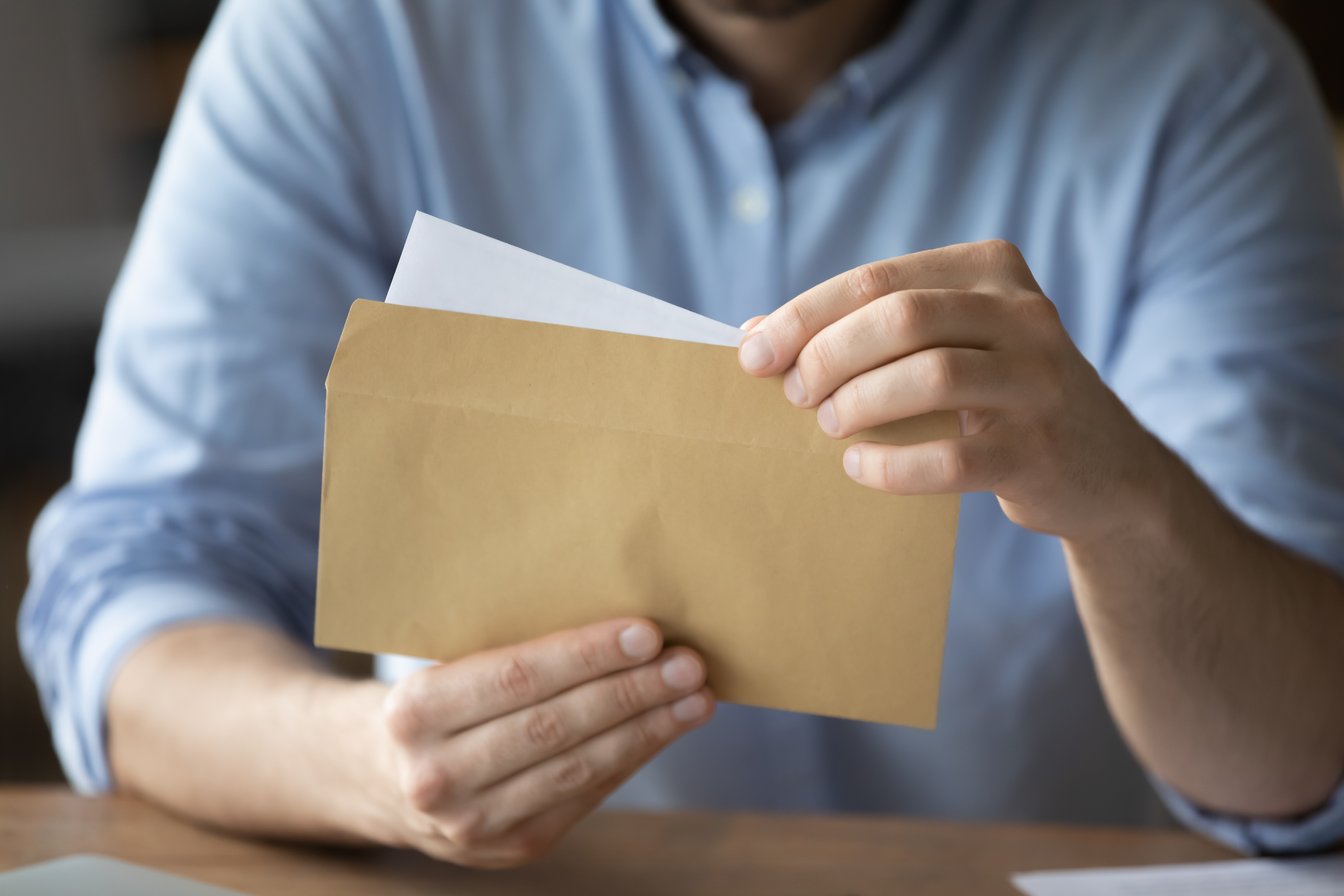 Businessman sitting workplace desk holding yellow envelope take out received paper letter notice sheet close up image business correspondence corporate news notification invitation concept