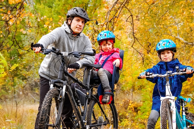 A dad and 2 children on cycles in a wood.
