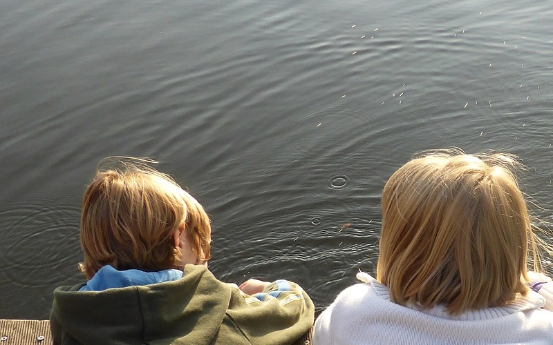 Two young children looking into an outdoor body of water.