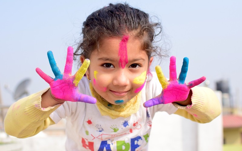 Young girl smiling with blue and pink paint on her hands.