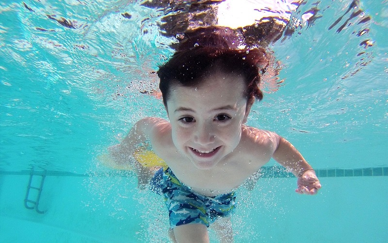 Young boy smiling under water in swimming pool.