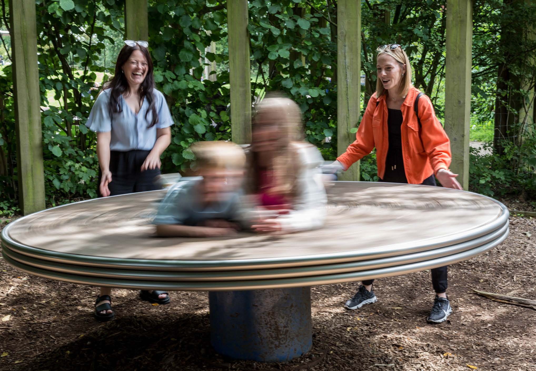Two people watching their children on a spinning table