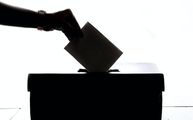 Silhouette of hand place vote into a ballot box.