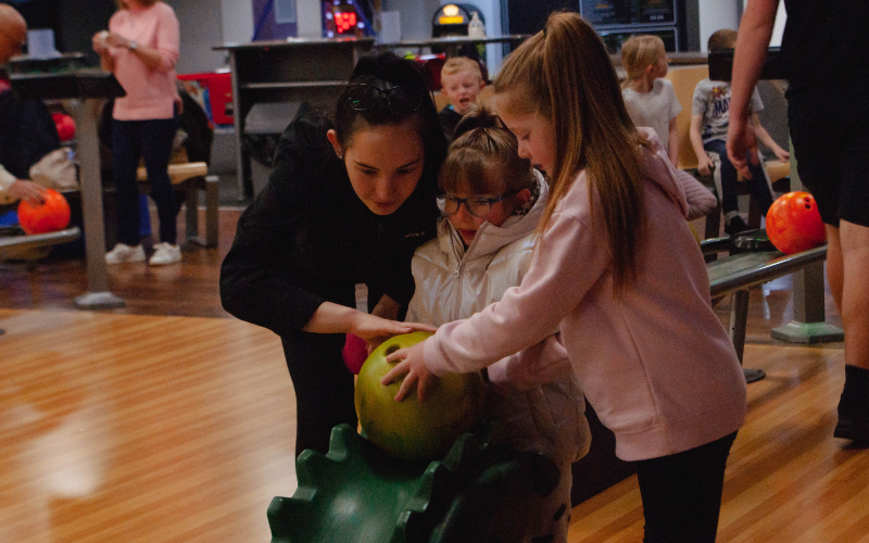 Children learning to bowl with holiday club staff.