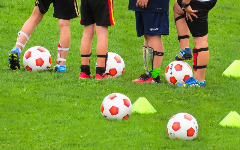 Children's legs on a grass pitch surrounded by footballs.
