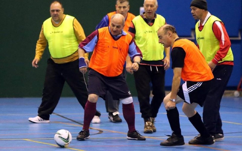 Men over 50s playing walking football indoors.