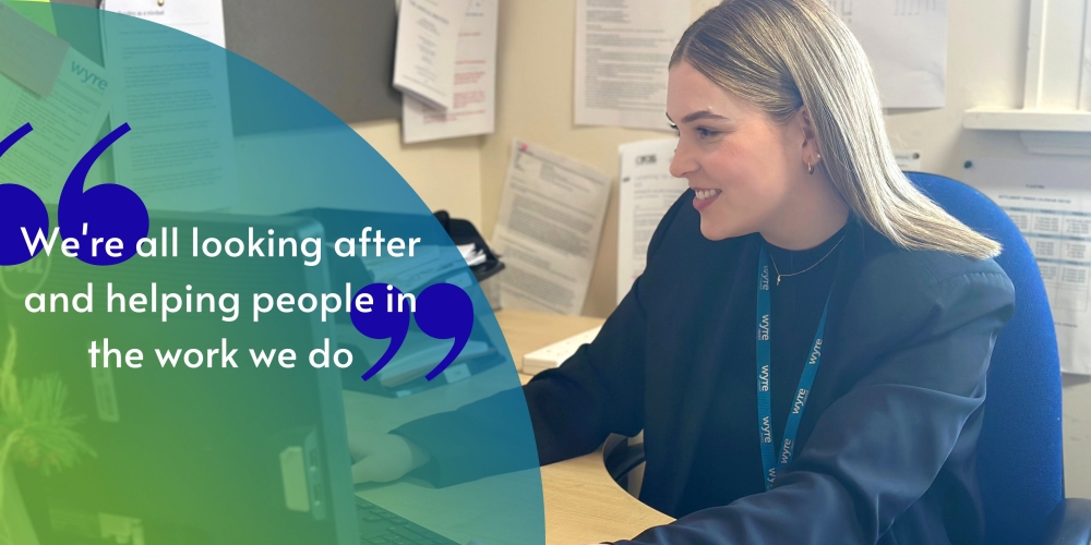 Marianne Unwin, Democratic Services Officer at Wyre council is sat working at her computer desk with the quote "We're all looking after and helping people in the work we do."