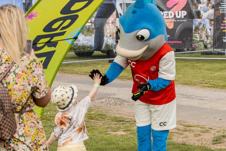 A child highfiving a person in a large blue fish costume.