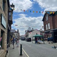 A road lined with shops. There's rainbow bunting and a blue sky with clouds overhead